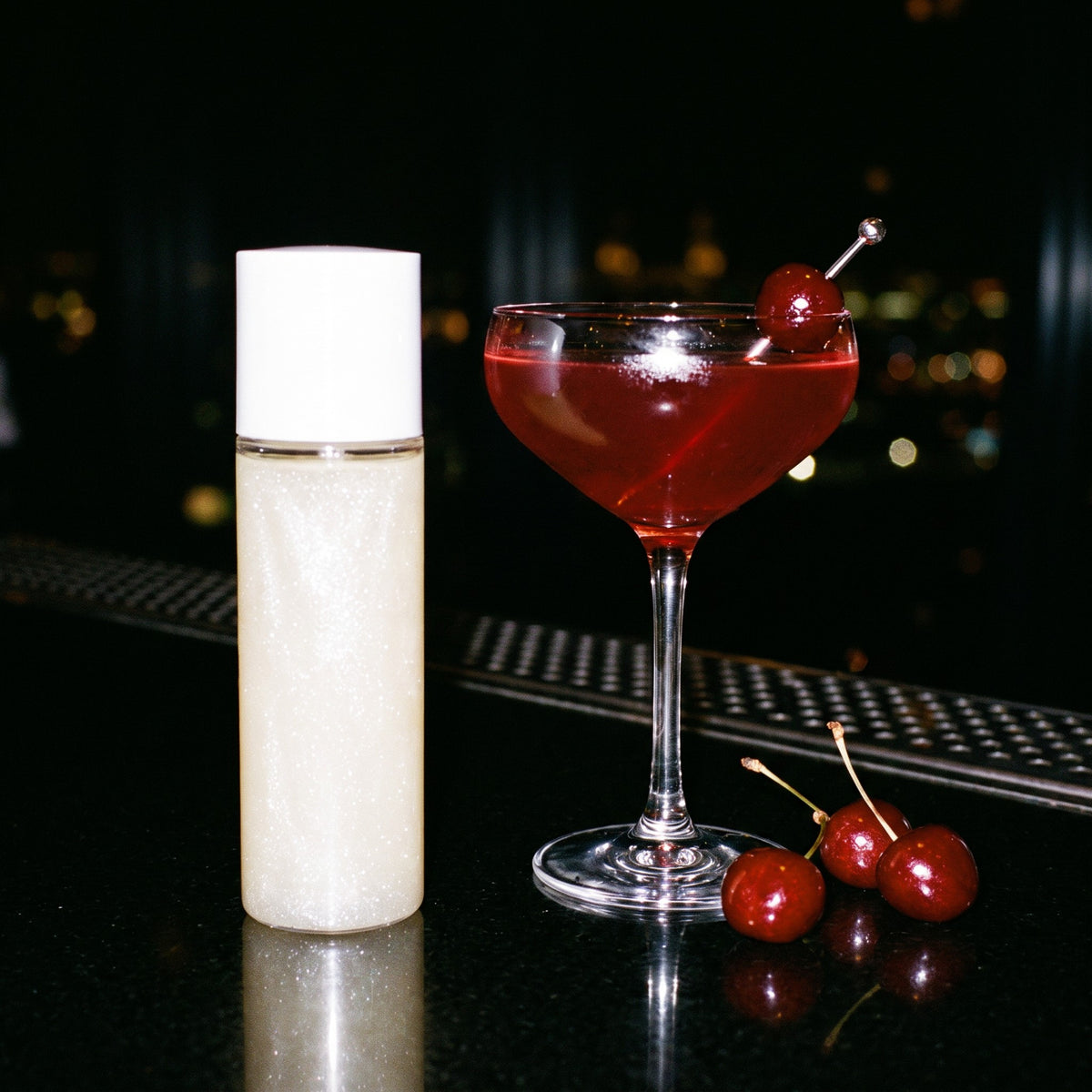 Ivory Pearl shimmer body oil beside a cherry cocktail